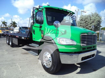 Green Freightliner M2 106 tow truck/rollback cab with flatbed, front chrome bumper, dual mirrors, dashboard windows, and side steps visible.