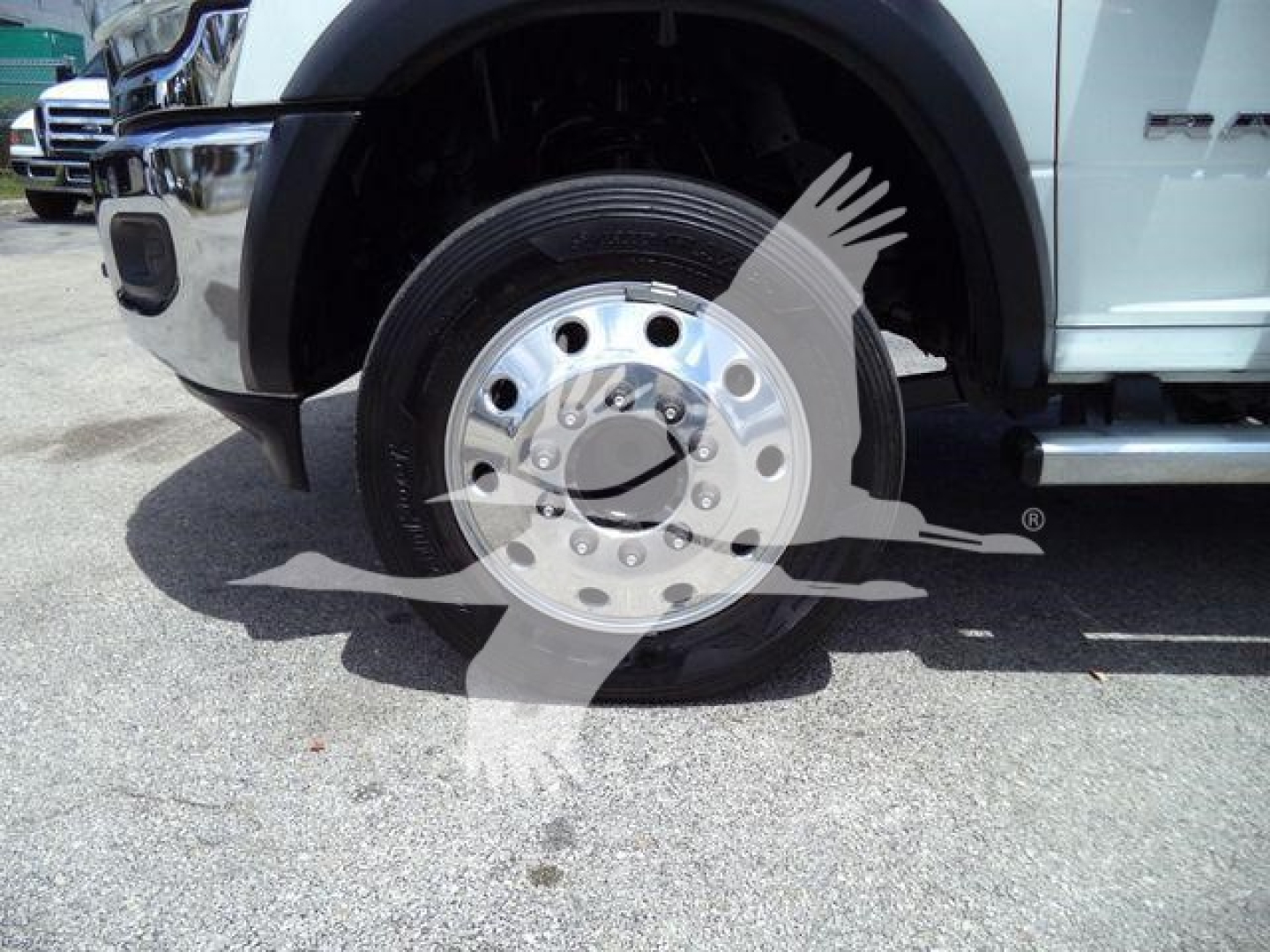 Truck front wheel showing wheel hub and tire, Ram badge visible on fender; partial front bumper and side step.