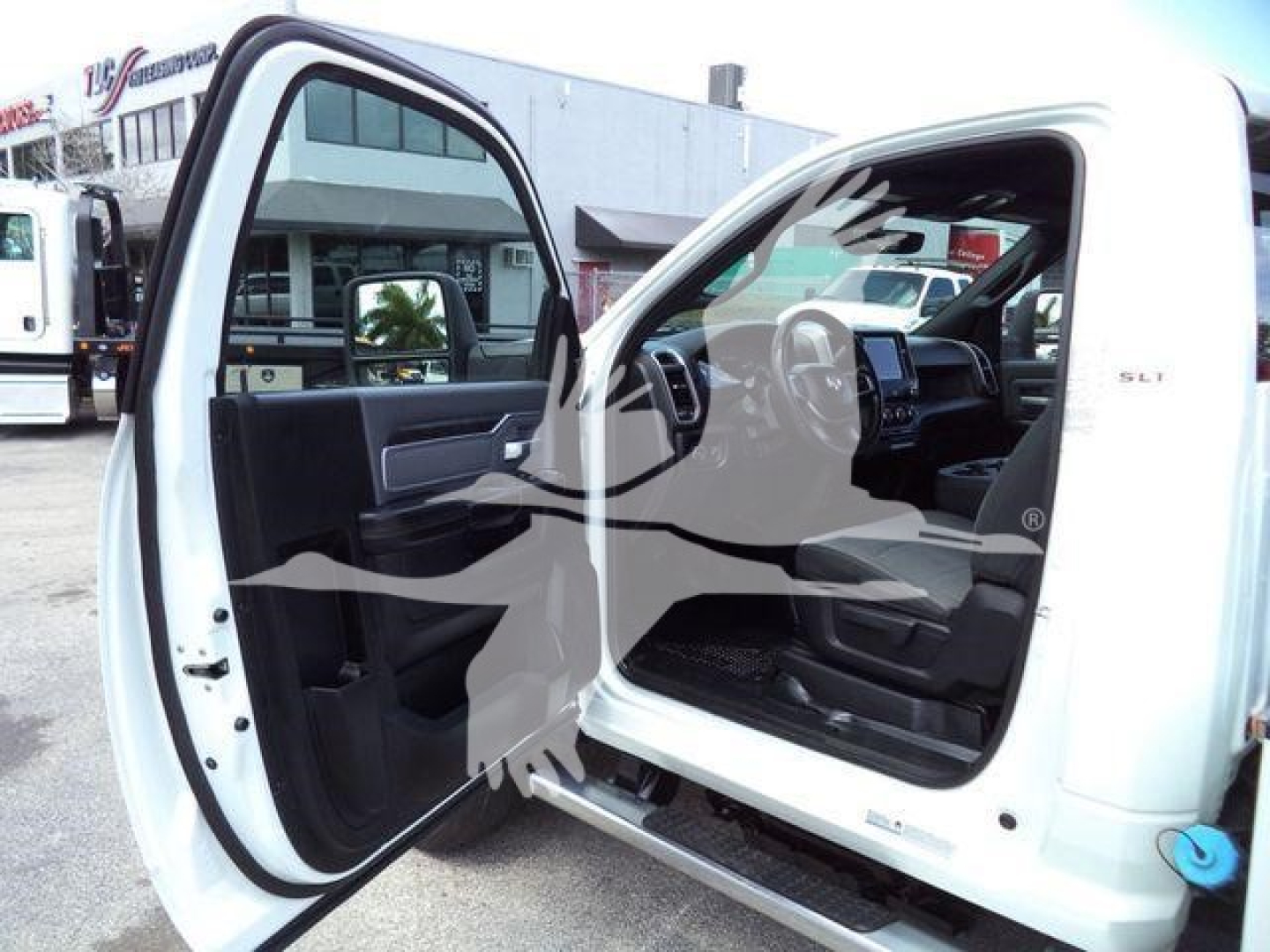 Truck interior: open front doors of a white Ram 4500 SLT showing steering wheel, dashboard, and center console; visible side step and door frame.