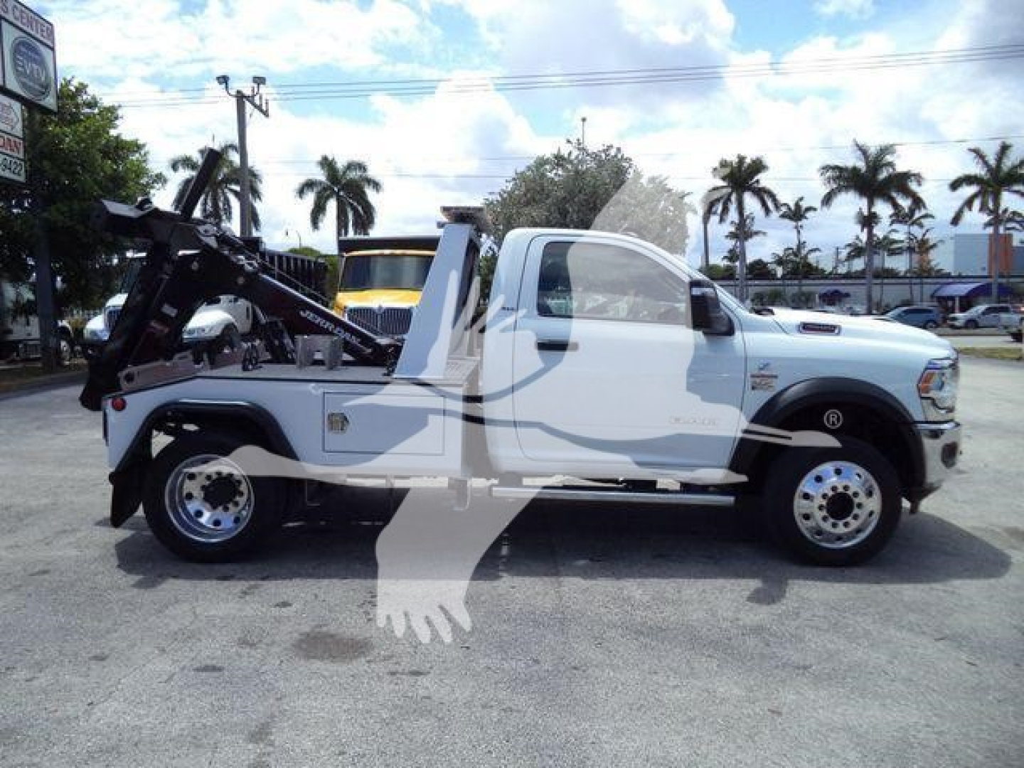 Truck bed with mounted winch and accessory crane on a white Ram 4500 SLT towing vehicle, side profile view in dealership lot.