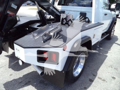 Ram 4500 tow truck rear side showing flatbed with winch and hydraulic crane, dual rear taillights, diamond plate bed, white exterior, wheel and tire visible.