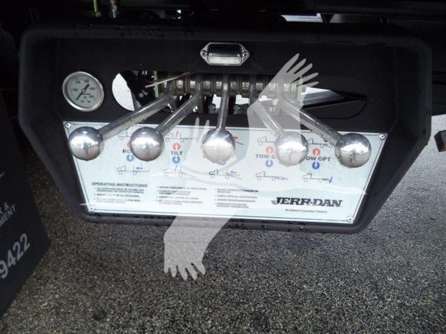 Panel and controls of a Jerr-Dan rollback tow truck, showing multiple chrome levers and a pressure gauge, with operating instructions label