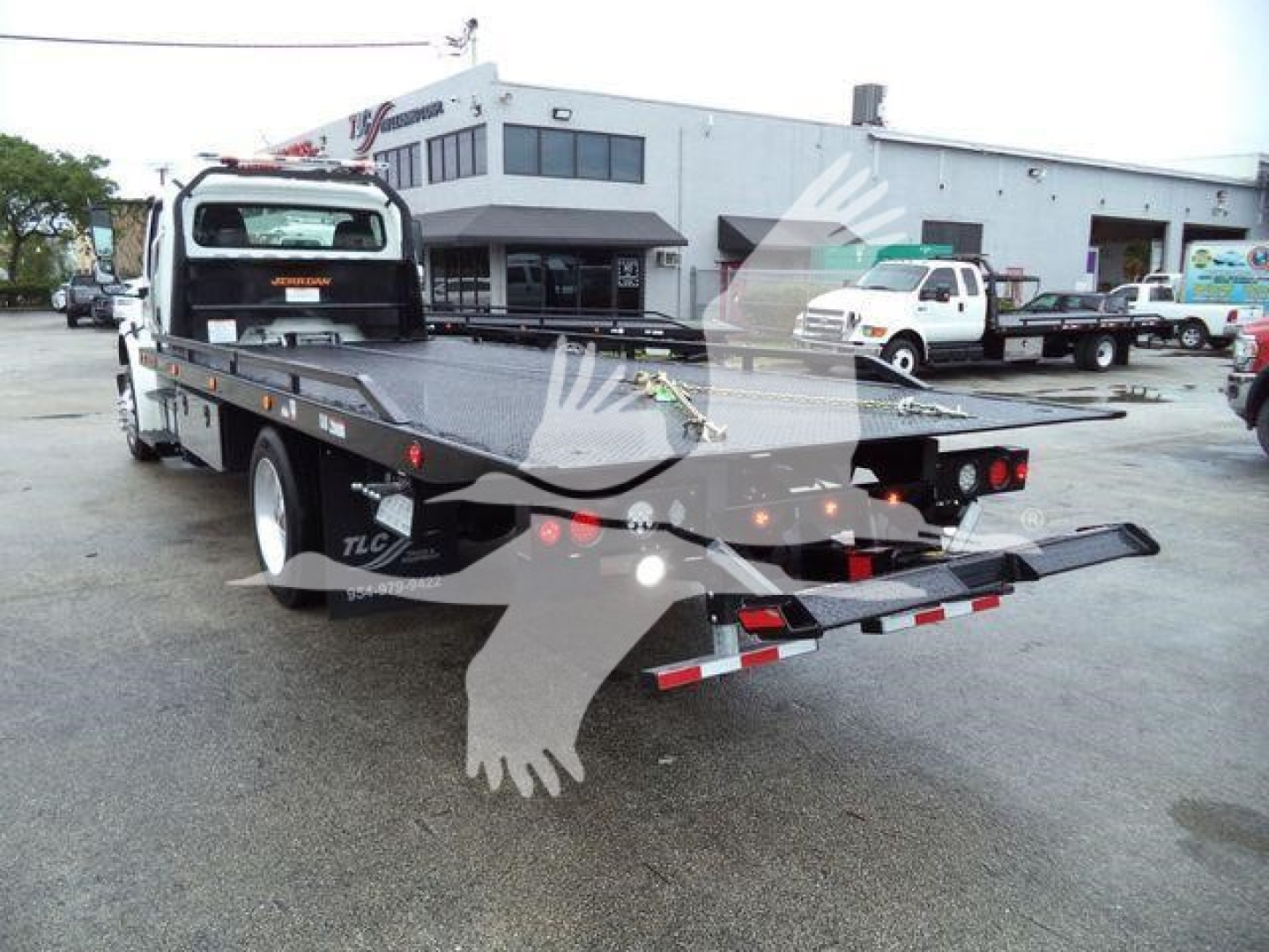Freightliner M2 106 rollback truck chassis with flatbed and rear loading ramp, viewed from rear-right in dealership lot.