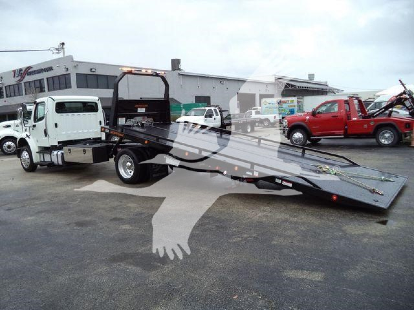 Freightliner M2 106 rollback tow truck with lowered heavy-duty flatbed in a dealership lot.