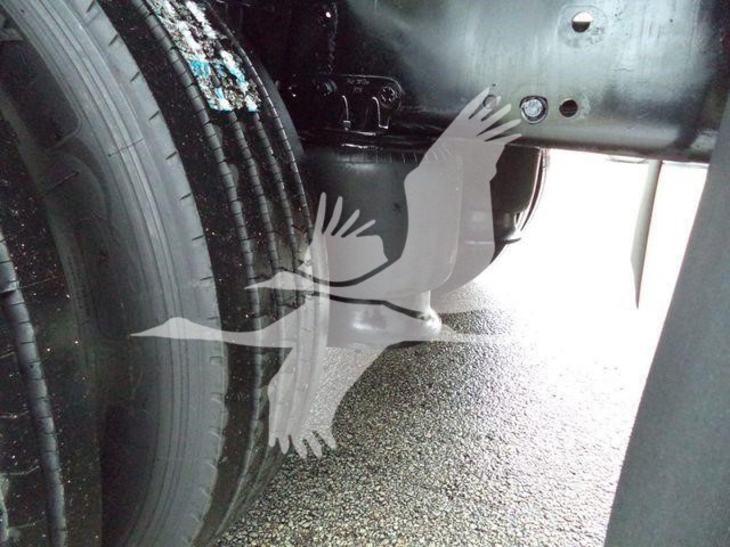 Truck undercarriage showing wheel and frame with a sticker and metal components. No legible brand or model text visible.