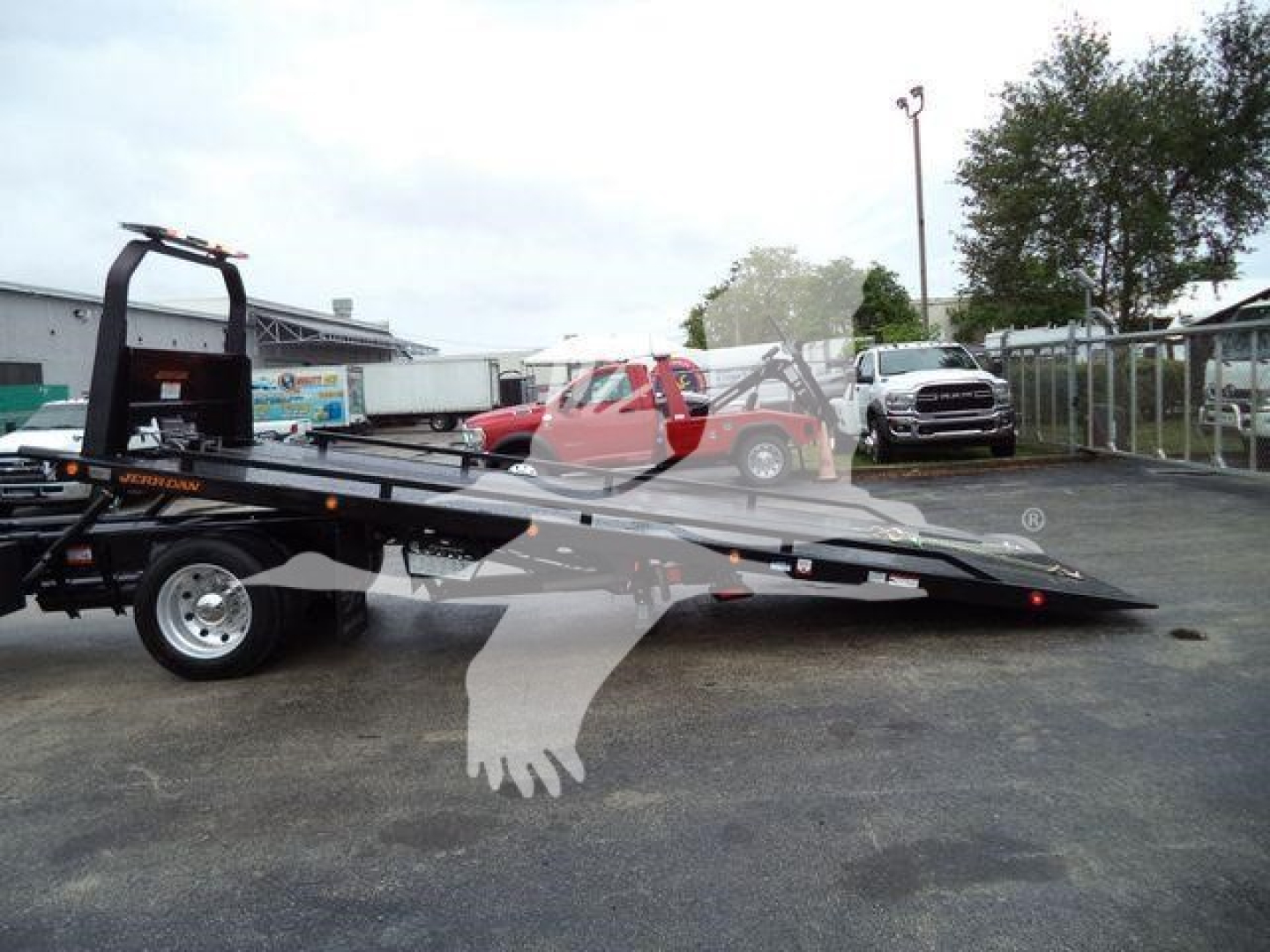 Flatbed rollback tow truck with loading ramps and hitch, Freightliner M2-style chassis, in a used vehicle lot.