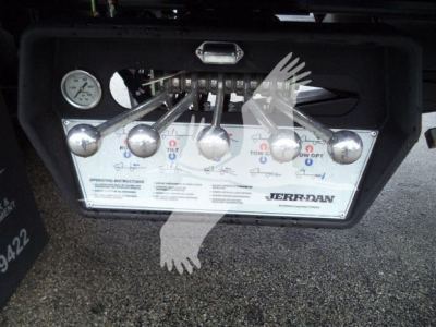 Panel and controls of a Jerr-Dan rollback tow truck, showing multiple chrome levers and a pressure gauge, with operating instructions label