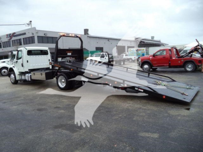 Freightliner M2 106 rollback tow truck with lowered heavy-duty flatbed in a dealership lot.