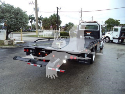 Truck bed of a rollback tow truck with folding ramps and rear lights visible; Freightliner-style cab in background.