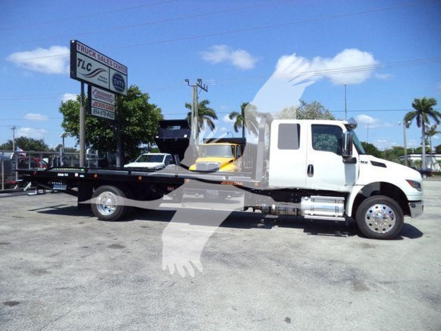 Tow truck/rollback with white cab and flatbed. Visible signs show TLC Truck Sales logo on a nearby sign. The truck appears new with stock number J18825.