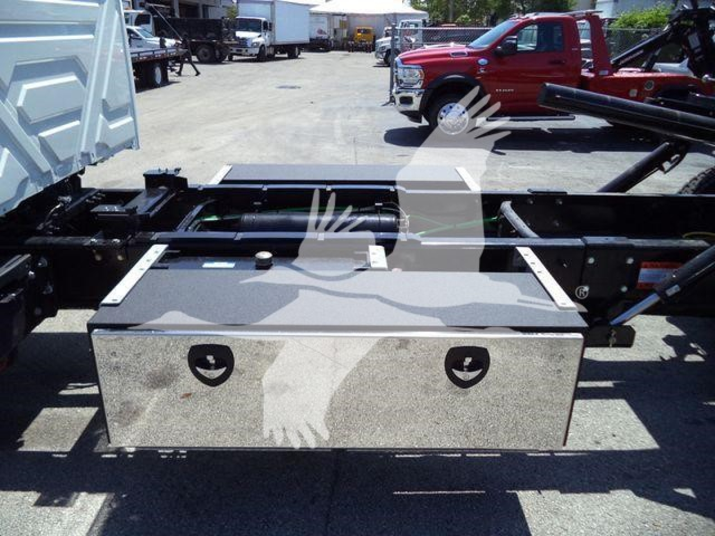 Truck chassis with storage toolbox mounted on a rollback frame and various vehicles in background.