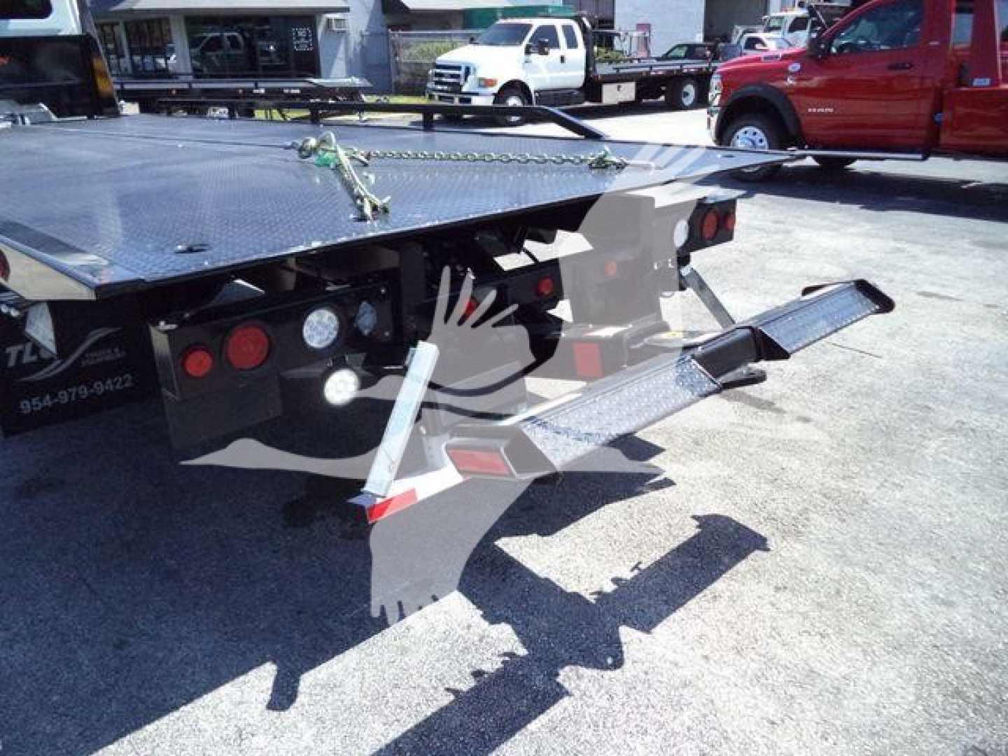 Tags and markings on a rollback truck bed and rear end including taillights, hydraulic components, and a fold-out loading ramp visible.