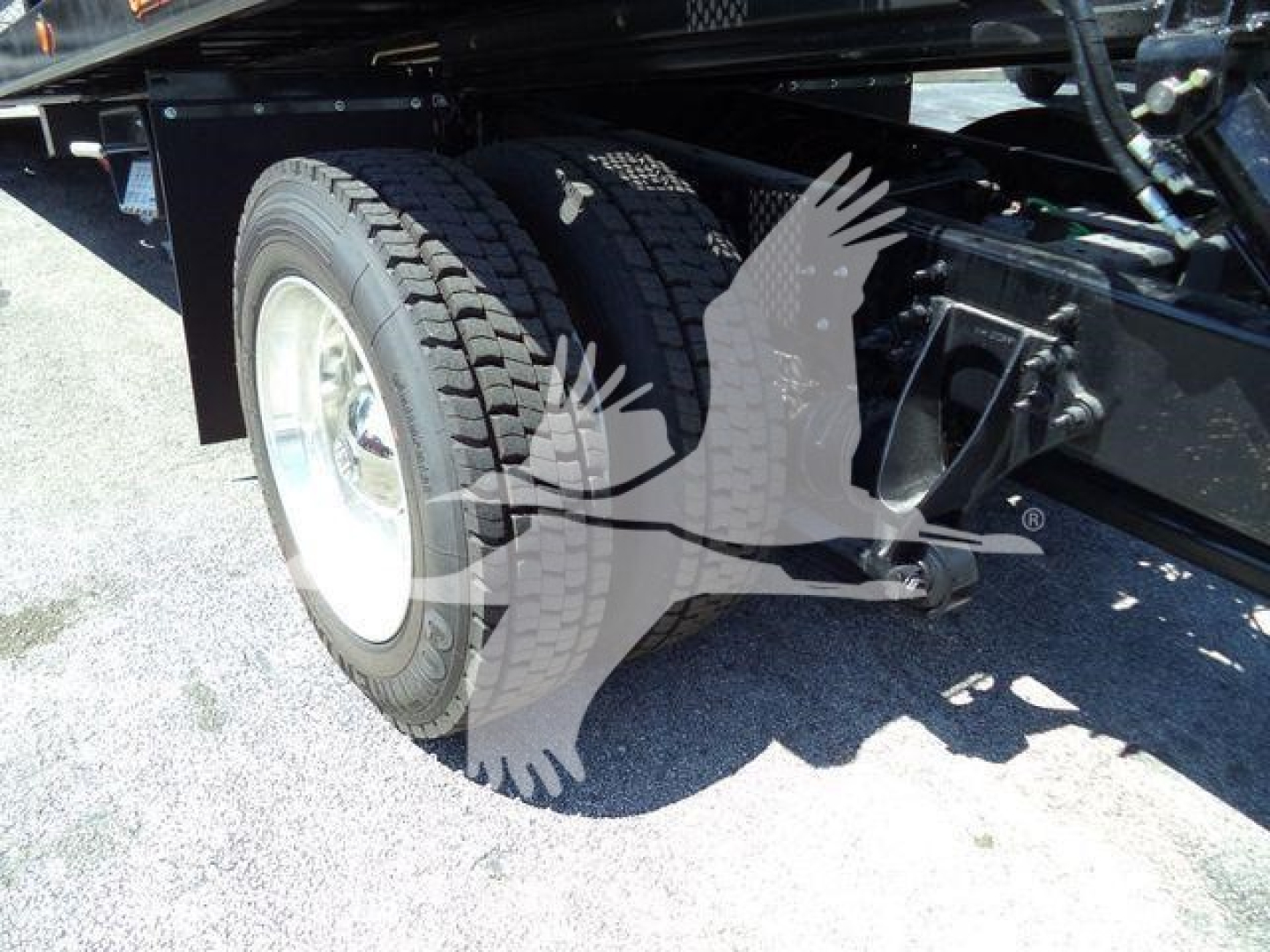 Truck rear wheel and chassis undercarriage with dual tires and suspension components visible.