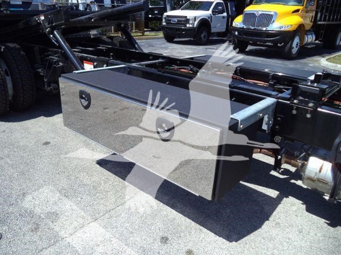 Truck flatbed chassis with an aluminum toolbox mounted on the frame, side view showing toolbox surface and mounting brackets.