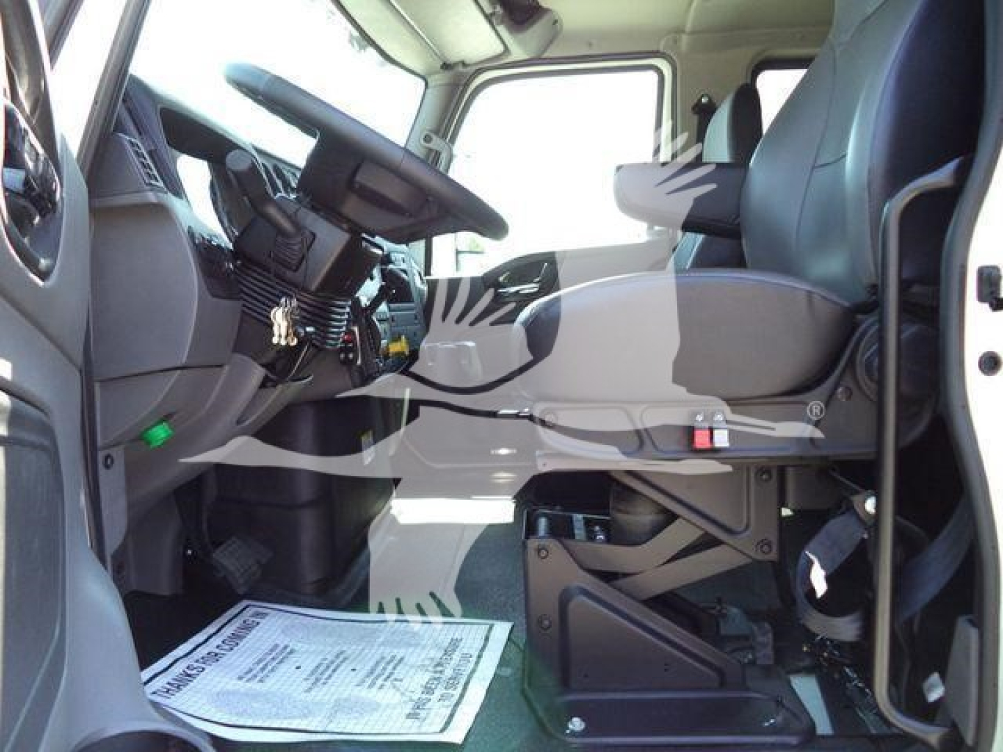Truck cab interior with steering wheel, driver seat, and dashboard visible in a right-hand drive configuration. Floor mat and seat mount hardware are seen.