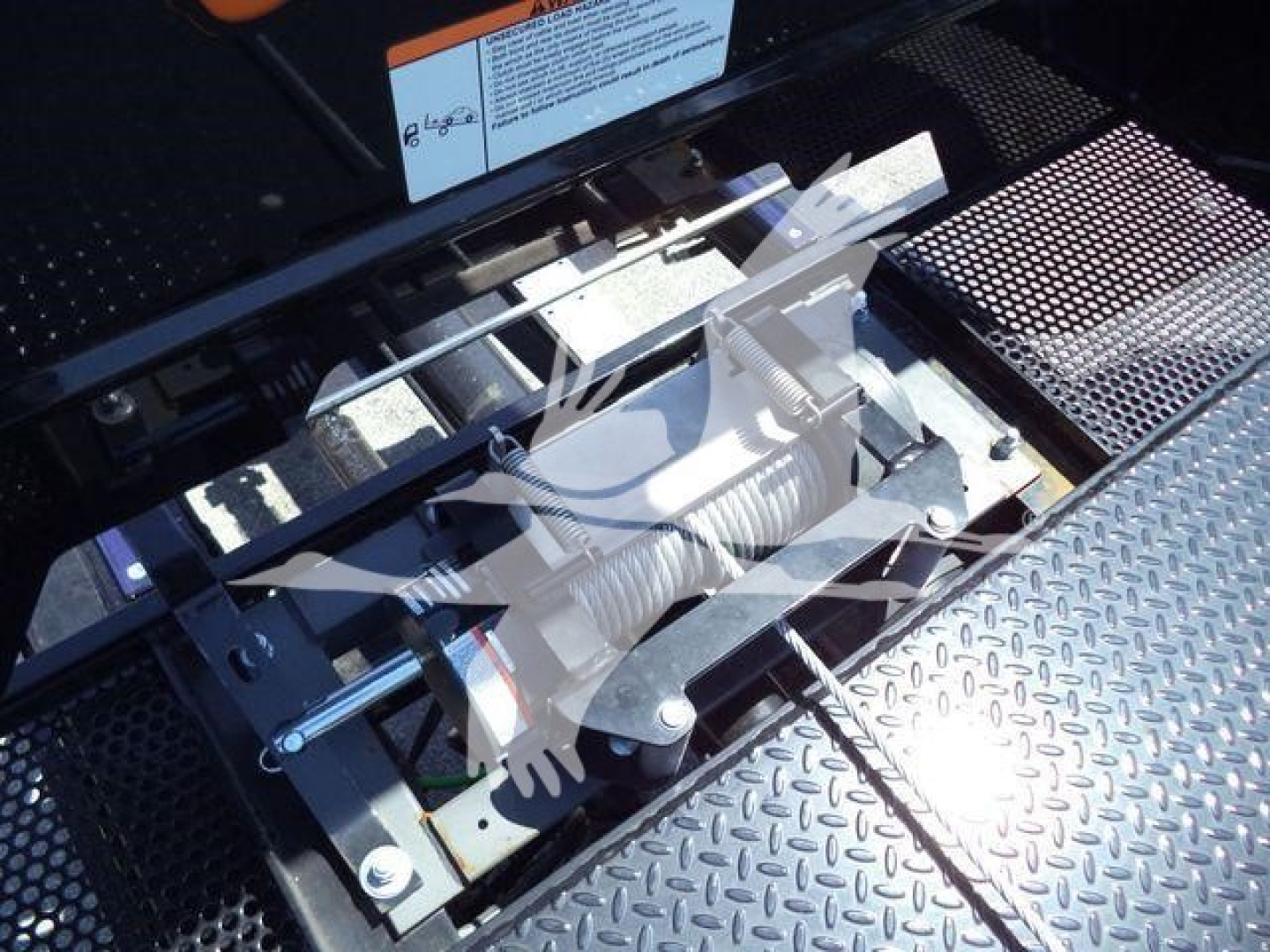 Truck equipment bay showing hydraulic air-ride or towing mechanism with metal linkage and coil spring components in a diamond plate platform.