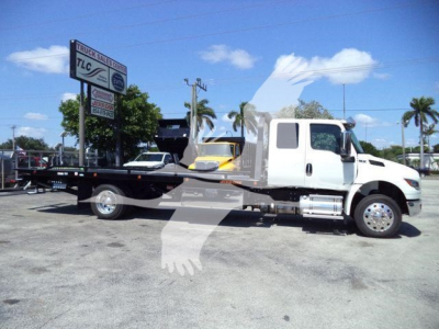 Tow truck/rollback with white cab and flatbed. Visible signs show TLC Truck Sales logo on a nearby sign. The truck appears new with stock number J18825.