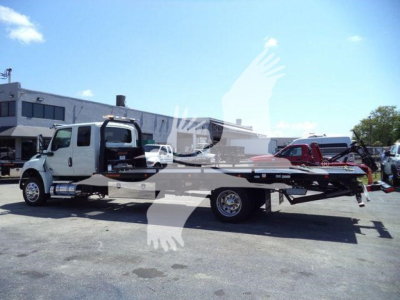Flatbed tow truck with rollback equipment in a lot; visible text on the truck may include branding but not legible; image shows a white International truck with a long flatbed and a red salvage crane.