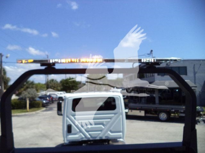 Truck cab viewed through a heavy-duty rollback truck bed frame with chrome bars and orange warning lights on top. Clear blue sky with clouds in background.