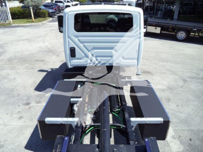 Truck chassis with flat bed and suspension components visible from rear, International MV cab in background, no text visible.