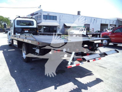 Truck rollback tow truck flatbed with hydraulic ramp in rear, International MV model, in a dealership lot.