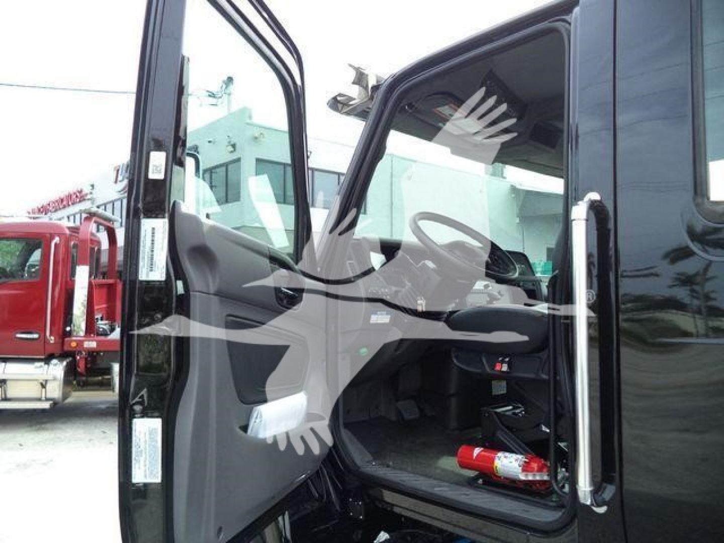 Cab view of a new 2026 International MV rollback truck showing open driver door and interior dashboard with a red fire extinguisher on the floor.