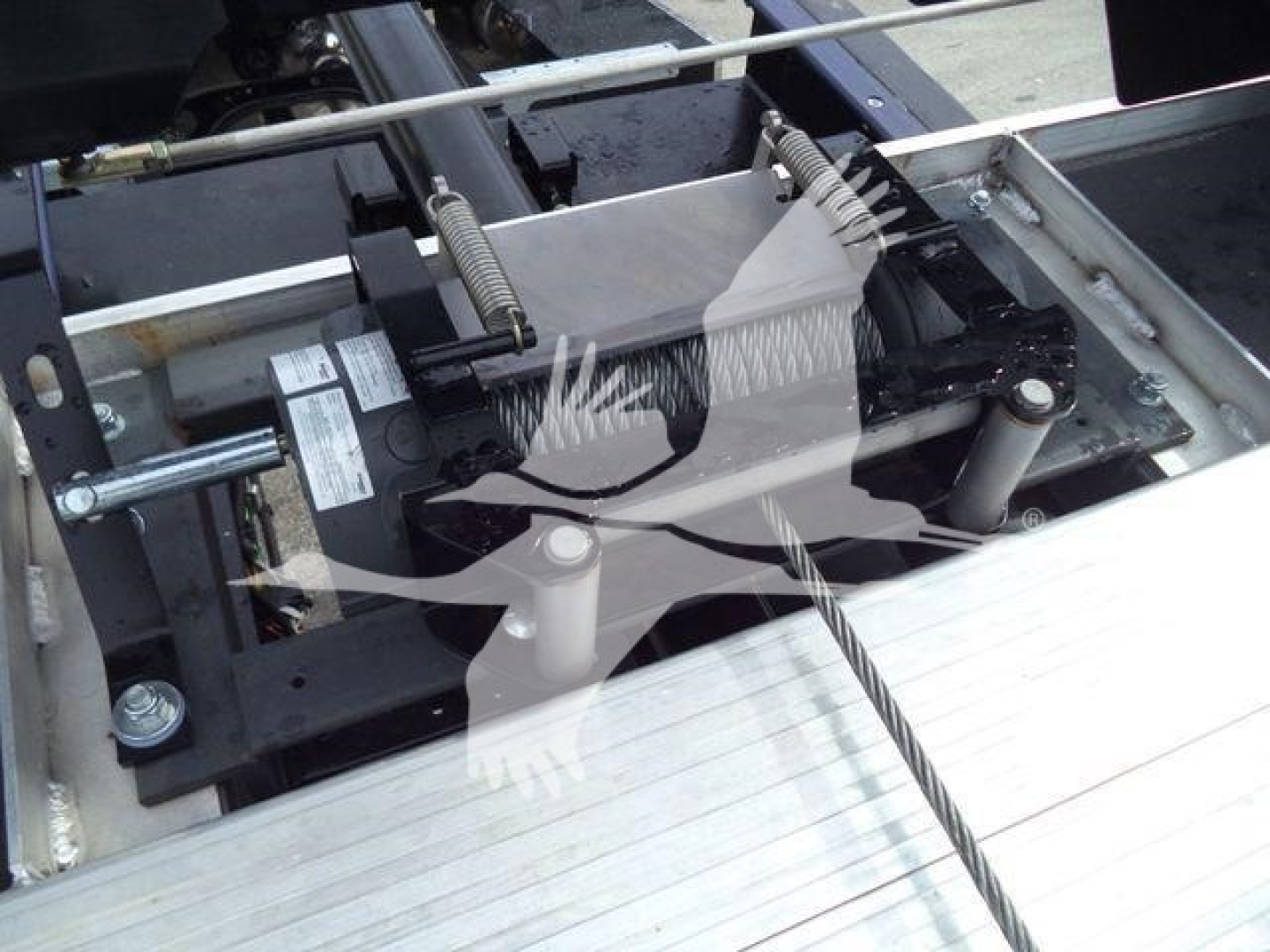 Truck rollback winch system with motor and cable assembly visible in a bay, factory labels on components.