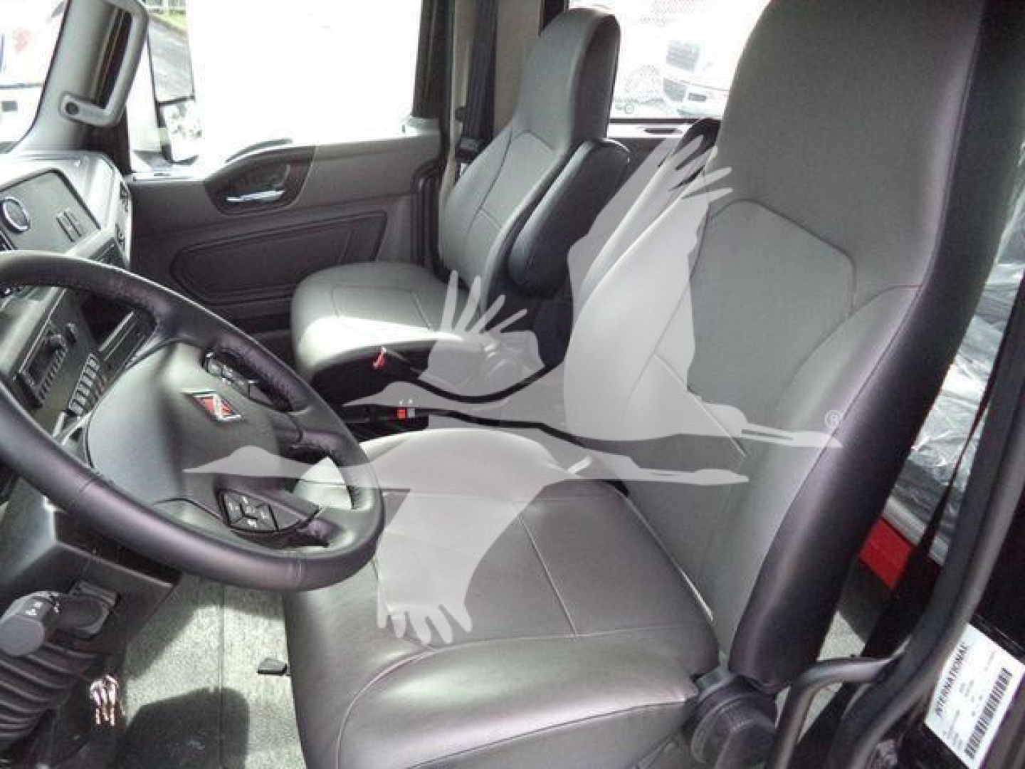 Interior of a 2026 International MV truck cab showing driver and passenger seats, steering wheel, dashboard, and doors.