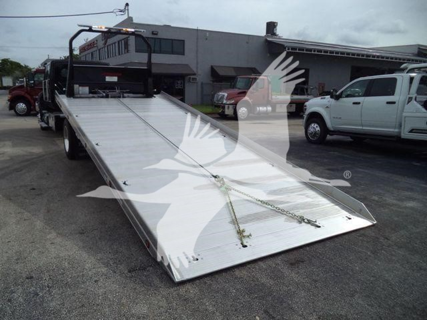 Flatbed rollback truck bed with aluminum deck and ramps, showing loading chain and hooks.
