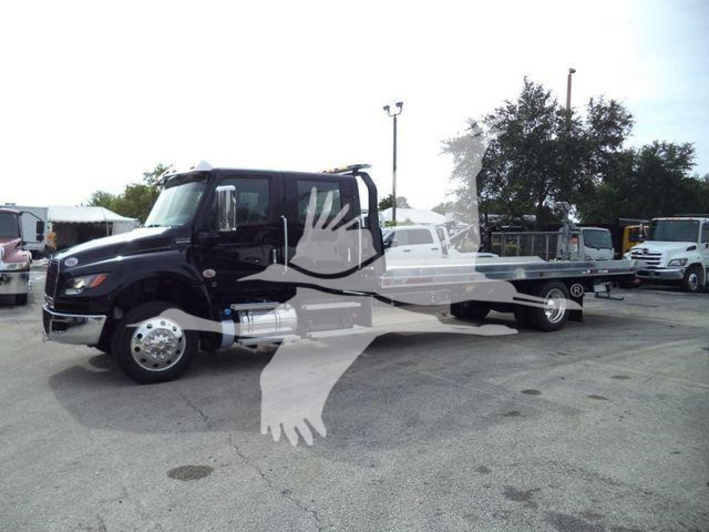 Tow truck with a flatbed, black cab, long chassis in a dealership lot; front grille and large chrome fuel tank visible.