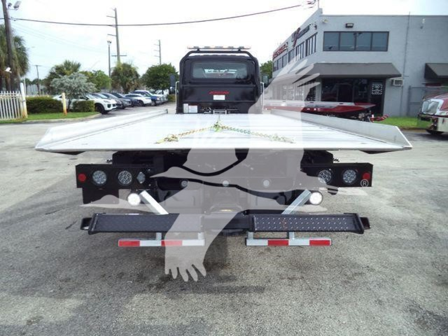 Truck bed or rollback equipment visible from rear; flatbed with lights and rear bumper; dealership lot in background.