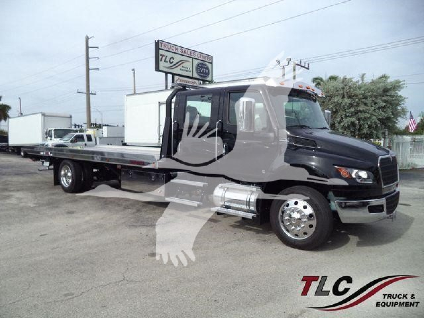 International MV truck side view showing rollback wrecker with long flatbed, black cab, chrome fuel tanks and wheels. TLC Truck & Equipment watermark.