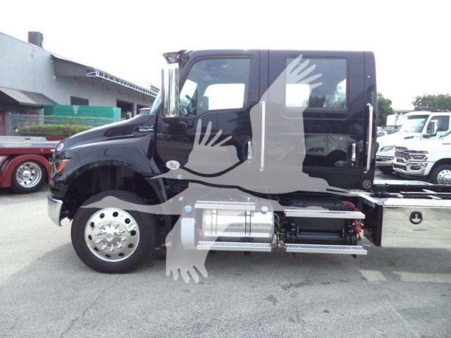Black International MV rollback truck side view showing cab with flatbed? and side fuel tank, step rail, wheel with chrome hubcap.