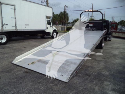 Flatbed tow truck with a long aluminum ramp and black cab, viewed from side showing hydraulic bed and rear loading ramp.