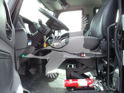 Interior of a new 2026 International MV truck cabin showing steering wheel, driver's seat, and mounted fire extinguisher on the floor near the pedal area.