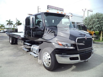 International MV truck showing a black heavy-duty hauler with rooftop clearance lights and chrome grille, flatbed rollback body, side steps, and large tires.