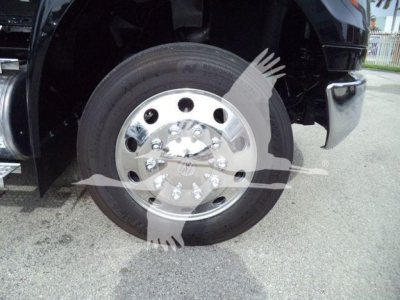 Wheel of a new 2026 International MV rollback truck showing a polished chrome hub and tire sidewall with tread, front fender and step area visible.