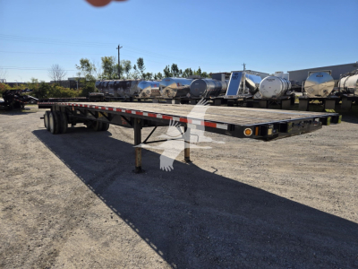 Flatbed trailer showing long deck with support legs and dual rear axles in a gravel lot.