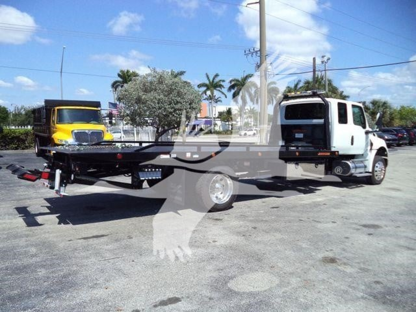 Flatbed rollback truck with a white cab and black trailer bed, International MV model, medium-duty tow configuration, visible stock number J18825FM in the background.