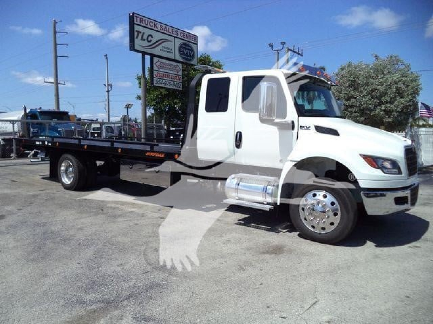 White International MV rollback tow truck with flatbed, side view showing cab and large chrome fuel tanks, sign in background, clear sky.