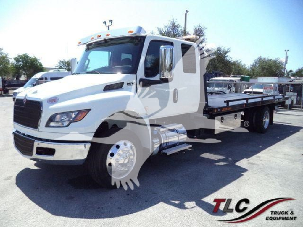 Truck cab and flatbed rollback in a dealership lot with International MV styling; no visible text on the cab or side panels.