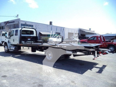 Flatbed tow truck on a dealership lot with a white cab and a black long flatbed, International MV model; stock number J18825FM visible in the background.