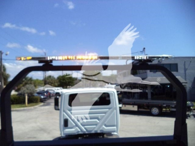 Truck body with rollback equipment frame visible; reflective window shows blue sky and a white cab in background.