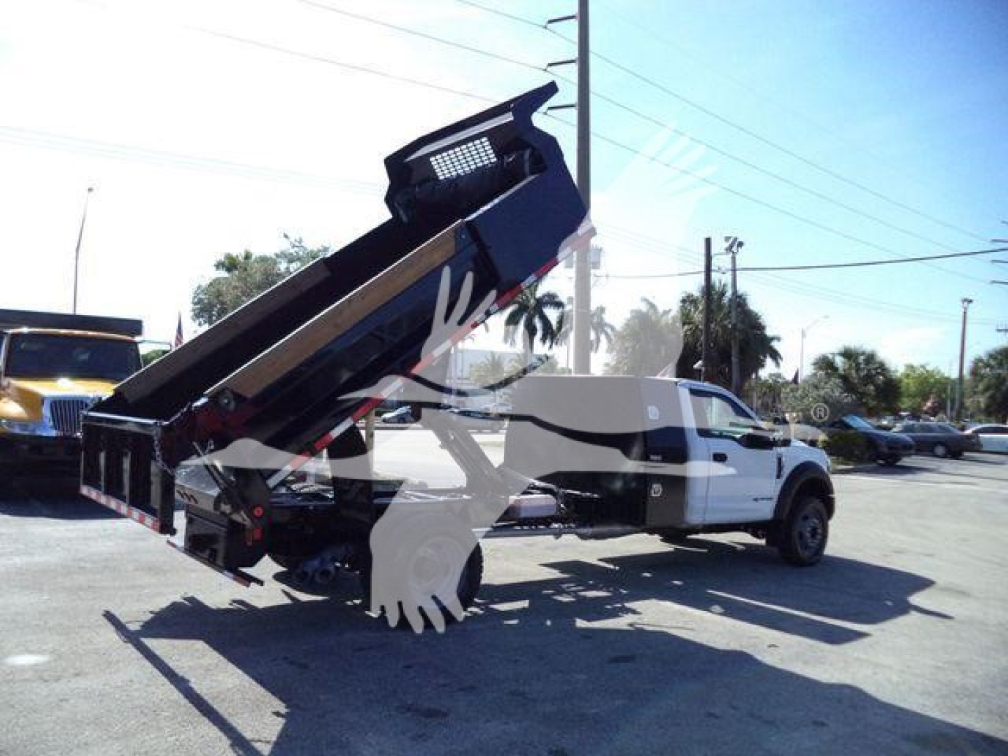 Ford F-550 dump truck in service with hydraulic dump bed raised, white cab, black dump body, roadside lot background.
