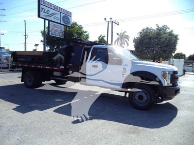 Ford F-550 dump truck with white cab and black dump body, side view in a dealership lot.