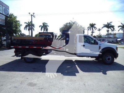 2019 Ford F550 dump truck side view showing white cab and red dump bed. Stock number T00690FM and category details visible in listing background.