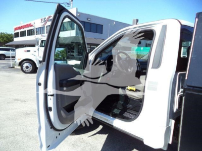 Interior of a white Ford F-550 dump truck with driver's door open, showing the dashboard and seating. Background shows other trucks and dealership lot.