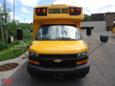 Front view of a yellow 2019 Chevrolet Express 4500 wheelchair school bus with extended mirrors and stop sign arms folded out.