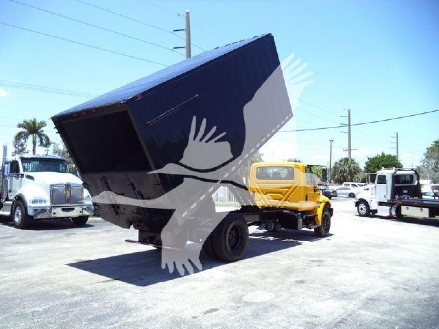Truck chassis with a raised dump bed showing a black dump container and surrounding vehicles in a lot.