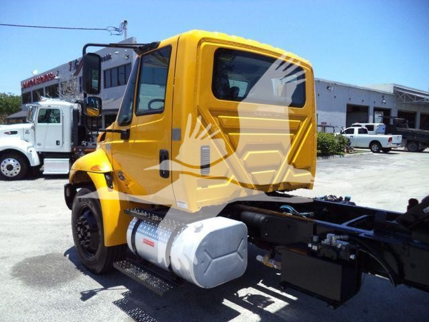 2019 International Durastar 4300 truck in yellow, side view showing cab, fuel tank, and chassis; background includes a white truck and industrial building.